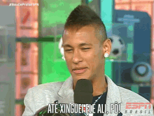 a man speaking into a microphone with the words " até xingue ele all po " on the bottom