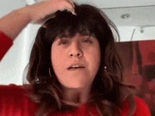 a woman wearing a red sweater is scratching her head