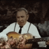a man in a white shirt and tie is playing a guitar in a dark room .