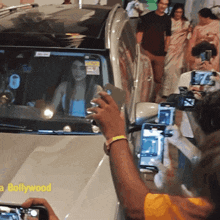 a man taking a picture of a woman in a car with a bollywood logo on the hood