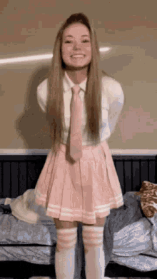 a girl in a pink skirt and tie is standing on a bed .