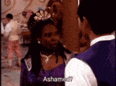 a woman in a purple dress and tiara is talking to a man in a white vest ..