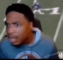 a man is sitting in front of a football field wearing a blue hoodie and a microphone .