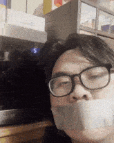 a man with glasses and duct tape on his mouth is standing in front of a microwave that has the time of 3:55