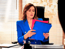 a woman in a blue jacket sits at a desk holding a folder