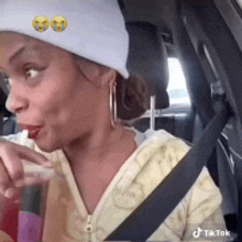 a woman wearing a beanie is sitting in a car drinking a drink through a straw