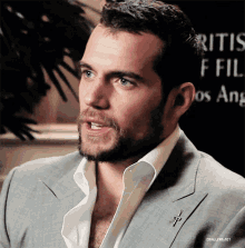 a man with a beard is wearing a suit and a white shirt with a cross pin
