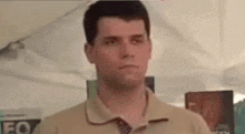 a man in a polo shirt and tie is standing in front of a tent .