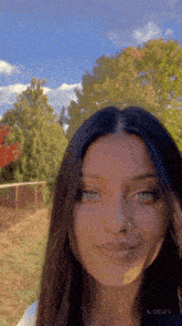 a girl with a nose ring is smiling in front of a blue sky and trees