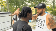 a man wearing a hat and a shirt that says sts is talking to another man in a boxing ring .