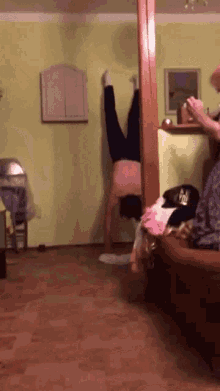 a woman is doing a handstand in a living room while a man sits on a couch