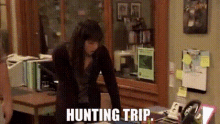 a woman is standing in front of a desk with the words `` hunting trip '' written on the screen .