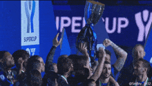 a group of soccer players holding up a trophy in front of a sign that says supercup