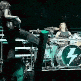 a woman is kicking a drum set on a stage while a man plays drums behind her .