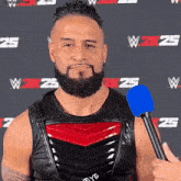 a man with a beard is holding a blue microphone in front of a wall that says 25