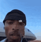 a man wearing a bandana is standing in front of an airplane .