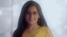 a woman wearing glasses and a yellow sari smiles for the camera .