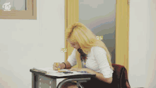 a girl sitting at a desk with a twice logo on the bottom right