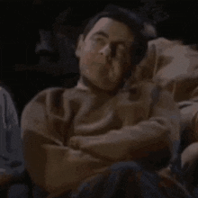 a man is sleeping on a couch in a dark room with his eyes closed .