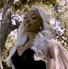 a woman with long white hair is standing in front of a tree .