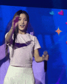 a woman wearing a white shirt that says ' i love you ' on it is singing into a microphone
