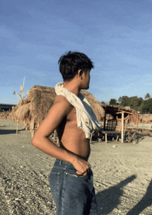 a man without a shirt is standing on a beach with a thatched hut in the background
