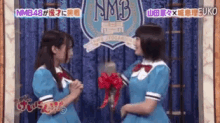 two girls are standing next to each other in front of a sign that says nmb on it .