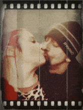 a man wearing a hat that says hanes kisses a woman on the cheek
