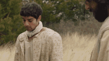 two men are standing in a field with one wearing a white shirt