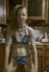 an older woman in a bikini is dancing in a kitchen