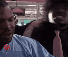 a man in a blue shirt is getting his hair cut by another man