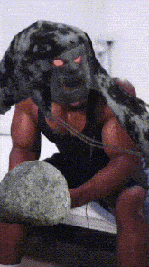 a man is sitting on a bed with a large rock on his head .