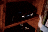 a person 's hands are reaching into a dark corner of a wooden shelf to pull something out