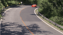 a red car is driving down a curvy road with trees on both sides