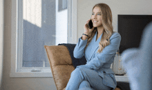 a woman in a suit sits in a chair talking on a cell phone