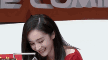 a woman in a red shirt is smiling in front of a sign that says ecom