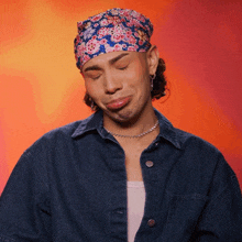 a man wearing a denim jacket and a floral headband is making a funny face