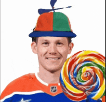 a man wearing a hat with a propeller is holding a large lollipop