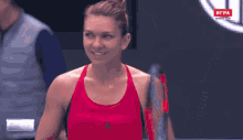 a woman in a red tank top holds a tennis racquet