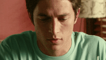 a close up of a man 's face wearing a green shirt with the letter t on it