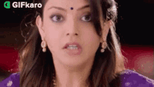 a close up of a woman 's face with a purple saree and earrings .