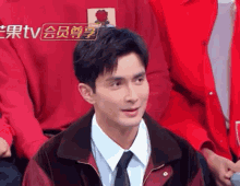 a man wearing a red jacket and tie is sitting in front of a sign that says tv