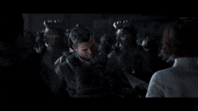 a man in a suit is standing in front of a group of soldiers and talking to a woman