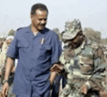 a man in a blue shirt is walking next to a soldier in a camouflage uniform .