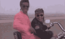 a man in a pink suit is riding a motorcycle next to another man .
