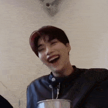 a young man is laughing with his mouth open while holding a cup .