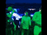 a group of people in green shirts are dancing in a dark room .