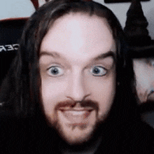 a man with long hair and a beard is smiling and making a funny face .