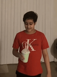 a boy wearing a red calvin klein jeans shirt holds a cup