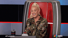 a woman is smiling while sitting in a chair with a nbc logo behind her